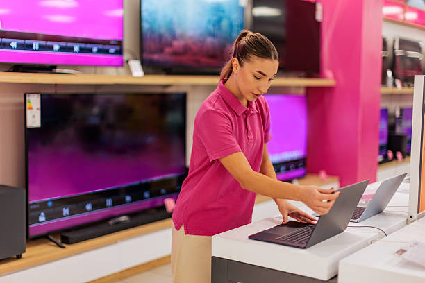 istock Sales Associate Setting Up a Laptop Display in an Electronics Store 2261077904