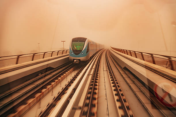 Modern metro train traveling on elevated tracks while the surrounding city is immersed in orange sandstorm haze. The scene highlights advanced urban mobility operating under challenging environmental conditions, connecting themes of resilience, climate adaptation, and future transportation.