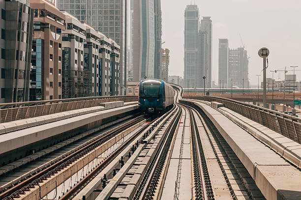 A sleek metro train travels through a dense urban corridor, framed by residential and commercial high-rise buildings. The image represents daily commuting, sustainable transportation, and the integration of rail systems within modern city landscapes.