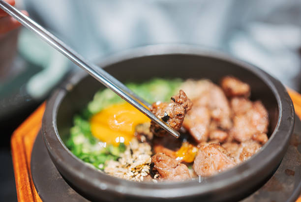 The image showcases a hearty dish of braised beef and potatoes, a comforting meal often found in various cuisines. The beef is browned and tender, indicating it has been cooked to perfection in a rich, savory sauce. The potatoes are soft and absorb the sauce, complementing the beef. The dish is presented in a pan that sits on a stove, suggesting it is ready to be served. The background is softly focused, featuring a person who might be preparing to enjoy this nourishing and satisfying meal. This photograph captures the essence of a traditional, home-cooked meal, inviting the viewer to appreciate the care and time put into its preparation.