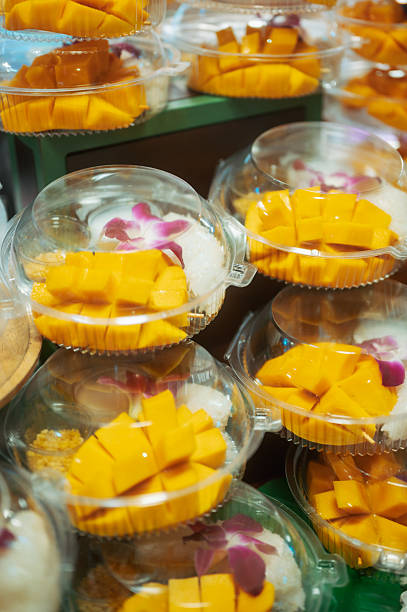 close-up of mango sticky rice dessert emphasizing sweet tropical flavors, traditional thai ingredients and modern takeaway presentation seen in busy asian markets, illustrating popular street food and culinary tourism trends.
