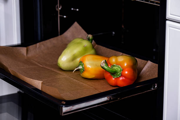 Three fresh bell peppers on brown baking paper inside open oven tray. Concept depicts healthy food preparation and organic vegetable roasting.