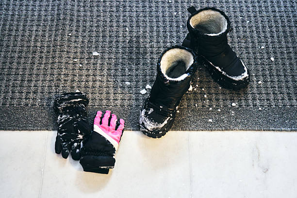Snowy winter boots and gloves drying on a grey doormat at the entryway after a cold outdoor walk, overhead view