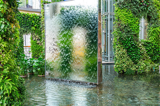 Biophilic design installation that combines vertical greenery, reflective water features and modern architecture in shopping mall in Bangkok city, Thailand. Vertical garden with waterfall. Fusion of urban design and sustainability