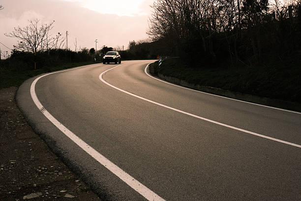 A car is driving down a curvy road. The road is empty and the car is the only vehicle on the road