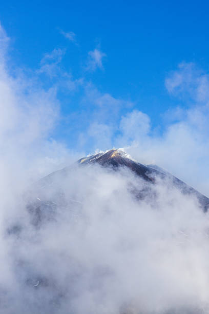 View of Mount Etna in Sicily covered in snow and ice under a bright, sunny sky. The iconic active volcano displays its icy slopes, rugged volcanic terrain, and striking winter landscape.