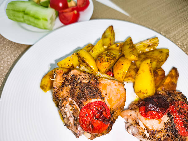 Delicious roasted chicken with potatoes and tomatoes seasoned with spices, served on a white plate, offering a healthy and flavorful meal