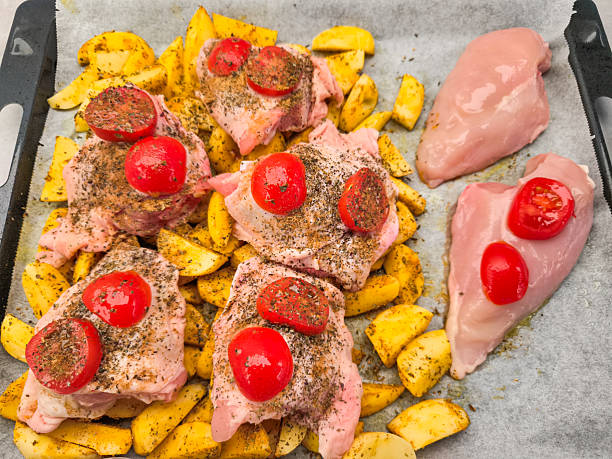 Chicken thighs and breasts seasoned with spices, potatoes, and cherry tomatoes, prepared on a baking sheet, ready for oven baking