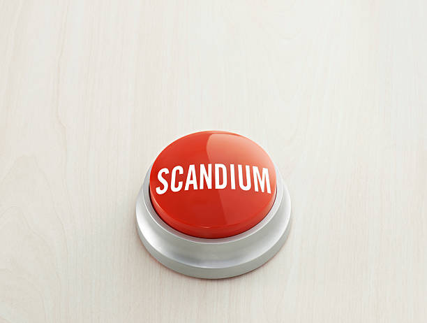 Red push button labeled scandium sits on a light wooden surface, symbolizing the importance of this critical mineral and rare earth element in modern technology and clean energy. This simple, isolated composition is ideal for topics such as mining, strategic resources, periodic table elements, and industrial materials in reports, presentations, or infographics. Full frame with copy space, horizontal orientation, suitable for editorial and commercial use.