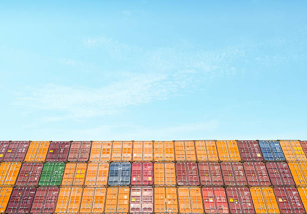 Rows of colorful shipping containers are stacked high against a clear blue sky, creating a geometric industrial pattern that represents global trade, logistics, and cargo transportation. The bright seaport scene is ideal for import export themes, supply chain articles, freight forwarding services, and international shipping concepts. Horizontal composition with ample sky copy space suitable for ads, reports, and editorial layouts.