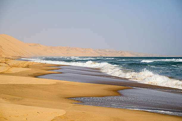 Beach at the Southern Atlantic Ocean coast with sand dunes in the background close to Walvis Bay in Namibia. It belongs to the Namib-Naukluft National Park.