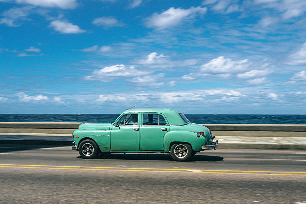 A classic mint-green car cruises along a seaside highway with the ocean and blue sky in the background. Havana vibes, retro style, travel nostalgia, and coastal scenery captured on a sunny day.