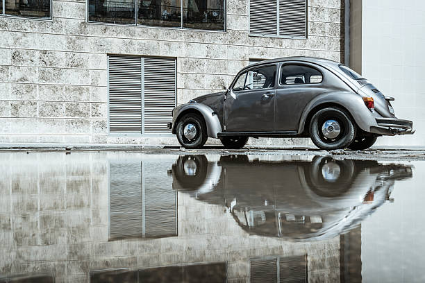 Havana, Cuba - February 23, 2017: A classic vintage Volkswagen Beetle parked beside a textured Havana facade, its wheel and body mirrored in a shallow puddle. Urban nostalgia and Cuban street atmosphere with moody lighting.