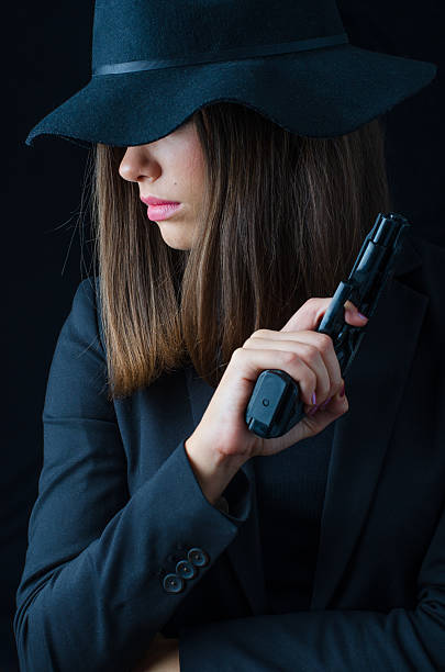 Mysterious woman in black clothes holding a gun posing in the studio.