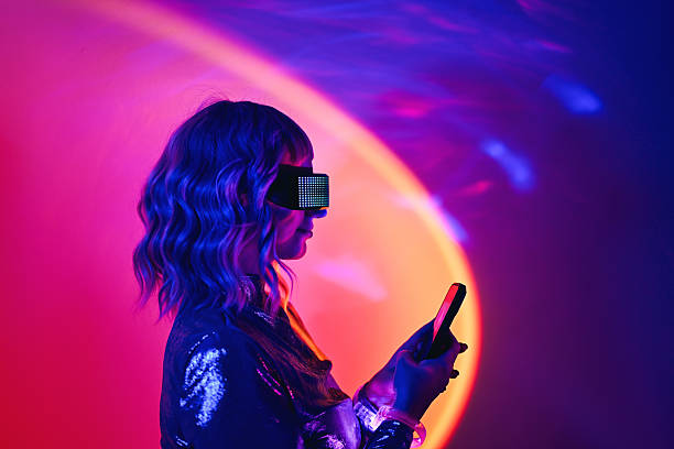Young woman wearing futuristic visor looking at her phone in neon light