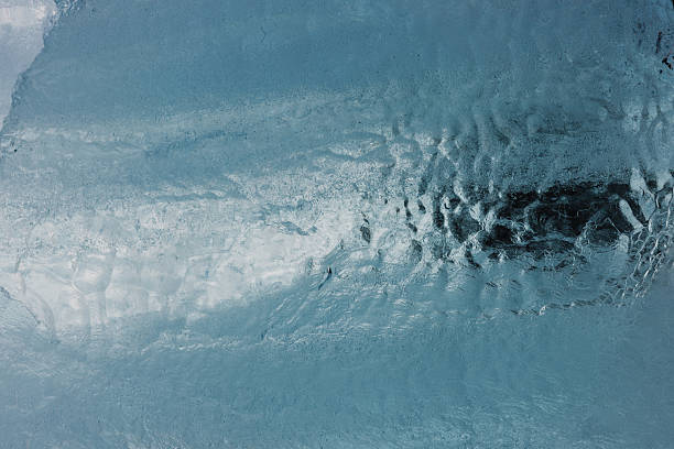 Large scale horizontal view of glacial ice displaying a textured surface with varying shades of blue, white, and dark shadows, capturing the cold, frozen environment of Icelandic nature