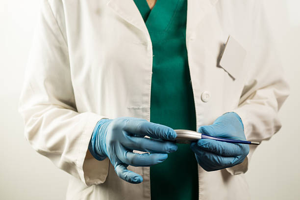 Hands of a medical professional in protective gloves holding a digital thermometer, ready to perform a clinical temperature measurement.