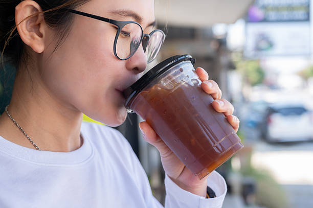 Asian woman while drinking an iced Americano coffee.