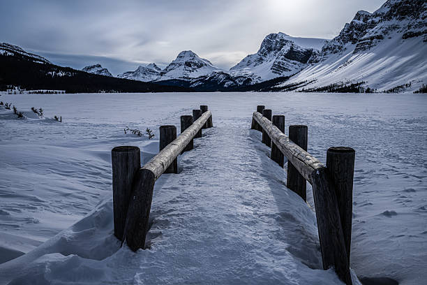 Canoes line up on dock overlooking water and mountains on cloudy day.
