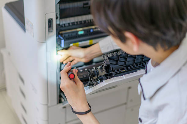 Close-up of a young Japanese man's hands performing maintenance on a copy machine in the office
