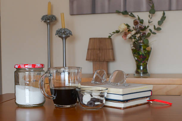Coffee cup with sugar, snacks and reading glasses on a stack of books, cozy study break scene on a wooden table evoking quiet, warm, relaxed reading and learning time