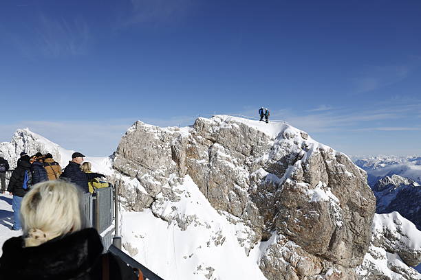 Zugspitze, Germany on November 18, 2025: Zugspitze, Germany on November 18, 2025: View of two young mountain climbers who reached the summit of Zugspitze, Germany’s highest peak, on a sunny day. The image captures the alpine scenery, snow-covered peaks, and the achievement of high-altitude mountaineering in the Bavarian Alps.