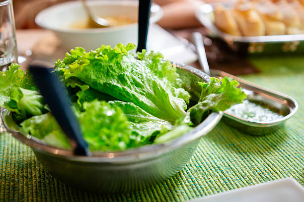 Fresh green lettuce leaves served in a metal bowl with tongs, ready for a healthy meal. Focus on healthy eating
