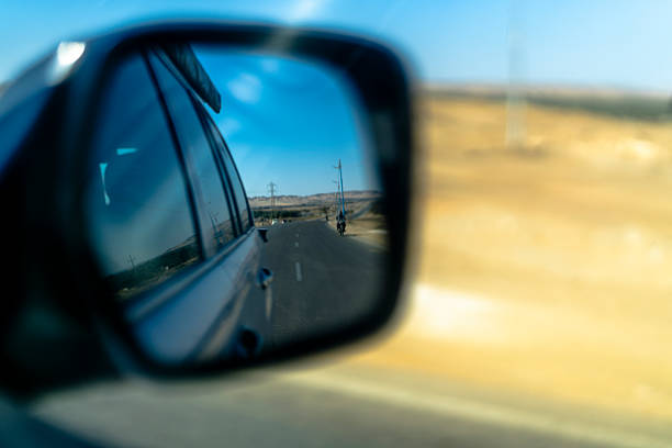 Desert road seen through a car side mirror in Giza, Egypt, showing travel movement, perspective, and a lone cyclist in an open arid landscape.