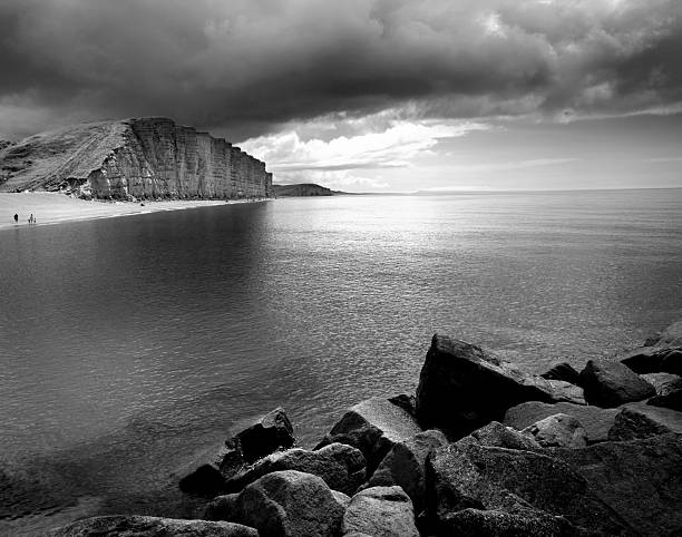 a very moody sky over the cliffs and sea at West Bay Dorset black and white