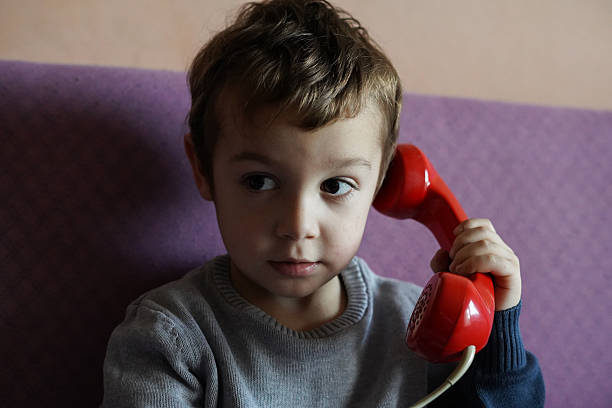 A 3-4-year-old boy exploring a landline phone while sitting on a sofa in a modern living room. The image captures the contrast between older technology like landline phones and the dominance of smartphones in today's world. This moment offers a nostalgic glimpse into the past as the child discovers technology in his own way