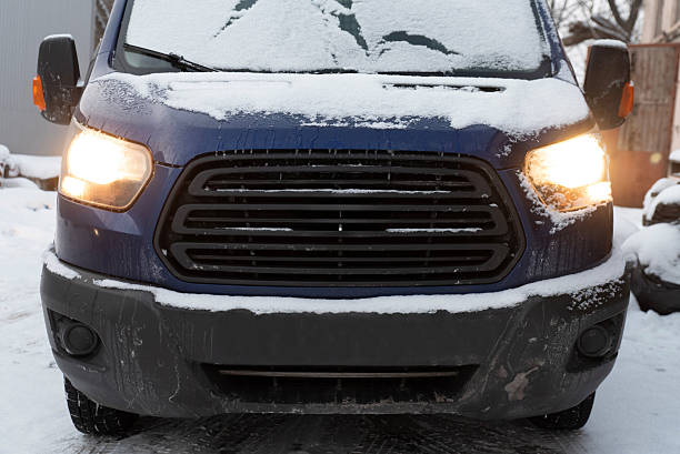 Front view of blue van covered in snow with headlights on