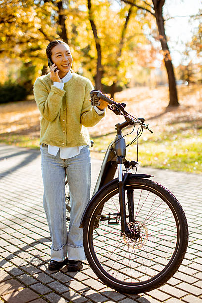 Woman enjoying an autumn day by the park with her bicycle and phone