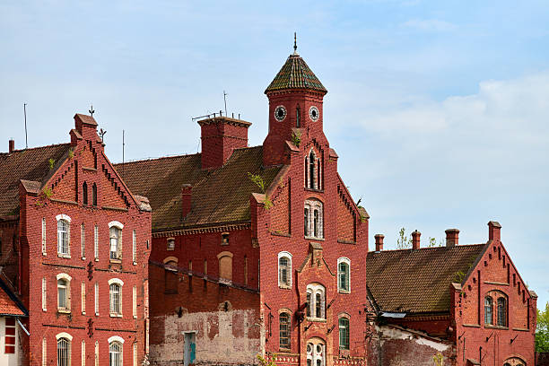 Abandoned castle in Tapiau, Gvardeysk shows traditional teutonic architecture. Red bricks and detailed stonework stand out against clear blue sky. Timeworn facade evokes past grandeur