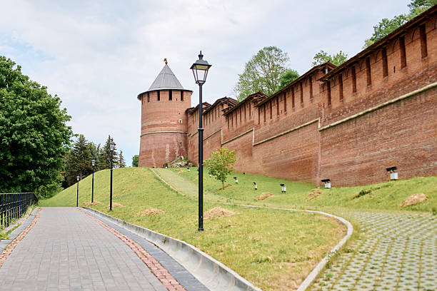 Iconic red brick walls and tower of Nizhny Novgorod kremlin under bright sky. Historic stronghold surrounded by lush greenery and cobblestone paths, offering majestic views