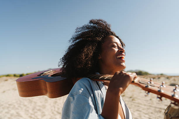 Photo of a beautiful African American woman, holding a guitar, on her way to the local beach