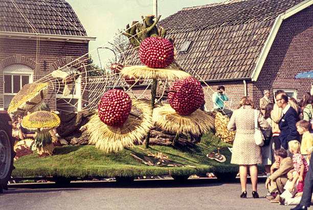 Historical slide showing a decorated float during the Harvest and Fruit Parade (Oogst- en Fruitcorso) in Tiel in the 1960s. The float, adorned with fruit, vegetables and natural materials, passes spectators lining the street. The annual parade in the Betuwe region is known for its elaborate fruit decorations and festive procession. September 1968, Tiel, Gelderland, The Netherlands.