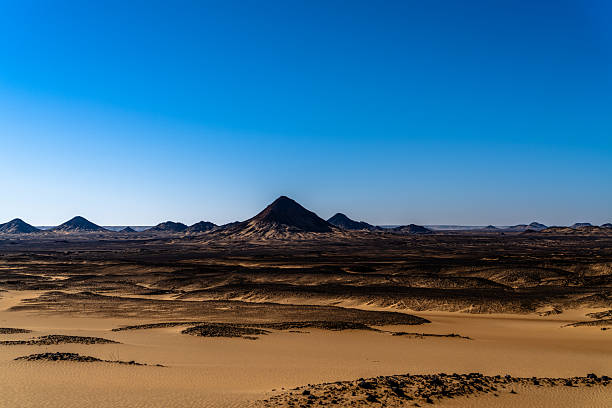 Wide desert landscape with dark volcanic hills and sandy plains under clear blue sky. Remote arid environment conveying isolation scale and natural power ideal for travel sustainability and climate concepts.