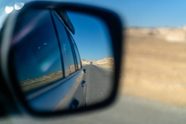 Road through arid desert reflected in a car side mirror with blurred sandy background. Conceptual travel image conveying journey movement and exploration in a remote landscape.