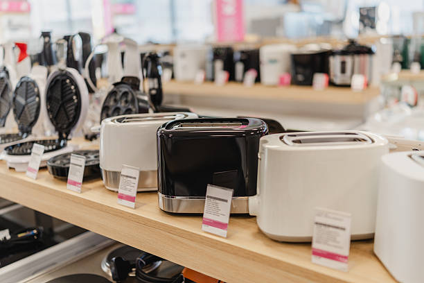 Row of electric toasters arranged on wooden shelf inside bright home appliance retail showroom.