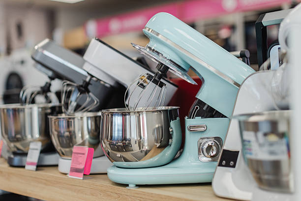 Multiple stand mixers arranged on shelf in modern kitchen appliance retail interior.