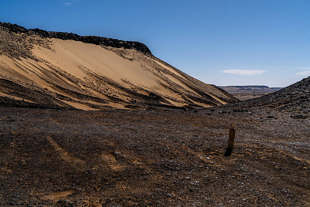 Angled view of a sand covered slope beneath a basalt ridge in Egypt's Black Desert near Giza, highlighting surface texture, erosion, and harsh climate conditions.