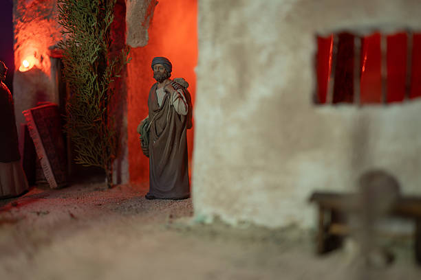 Spain. Miniature of a traveler with a satchel, walking through a narrow nighttime alley in a detailed Christmas nativity scene. The scene captures the quiet of the night and the historical atmosphere of the traditional town of Bethlehem, bathed in a warm glow that evokes the serenity of Christmas.