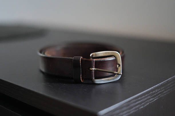 Brown leather belt rolled on dark surface. Classic fashion accessory and clothing detail close up.