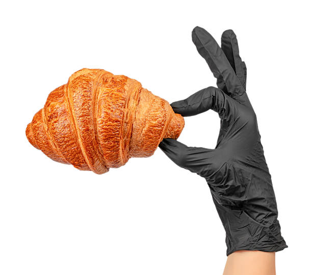 Fresh croissant held by hand in black glove isolated on white background