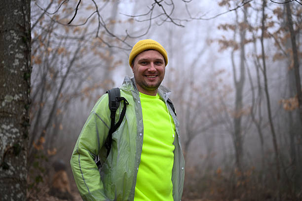 Man wearing yellow hat and raincoat hiking and enjoying nature in misty woods