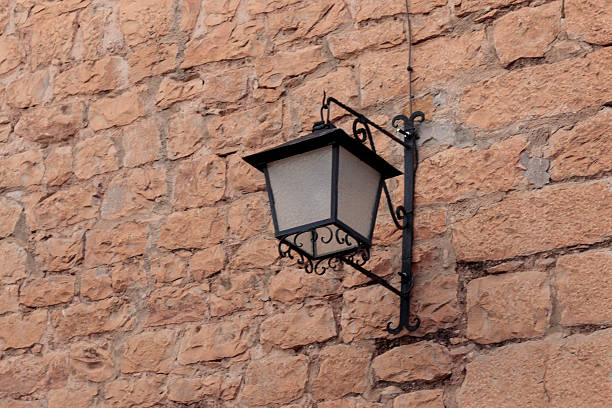 Wrought iron street lantern illuminating a textured stone wall