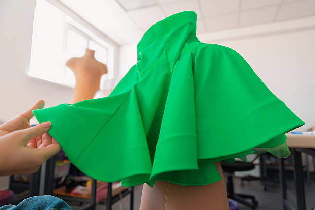 Hand draping green fabric, creating a new design on a dress form in a bright studio