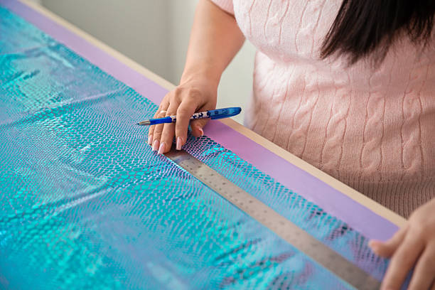 Person's hands holding ruler and pen, marking blue textured fabric for裁縫