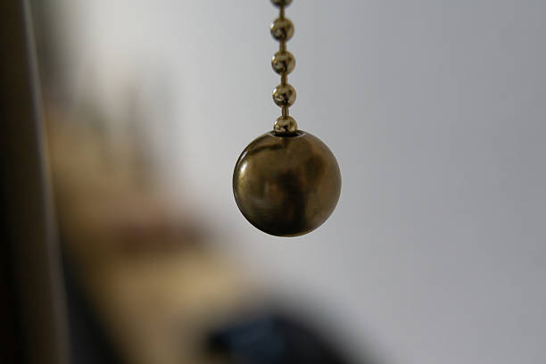 Close-up of a metallic ball attached to a chain, commonly used for blinds or light controls. The shallow depth of field creates a soft blurred background, emphasizing texture and minimal design. Suitable for concepts related to interior details and household mechanisms.