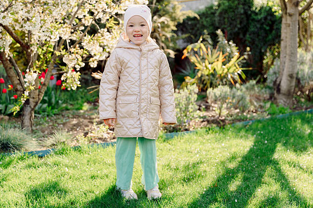 Smiling toddler standing in a blooming spring garden, sunlight and vibrant greenery creating a joyful family moment.